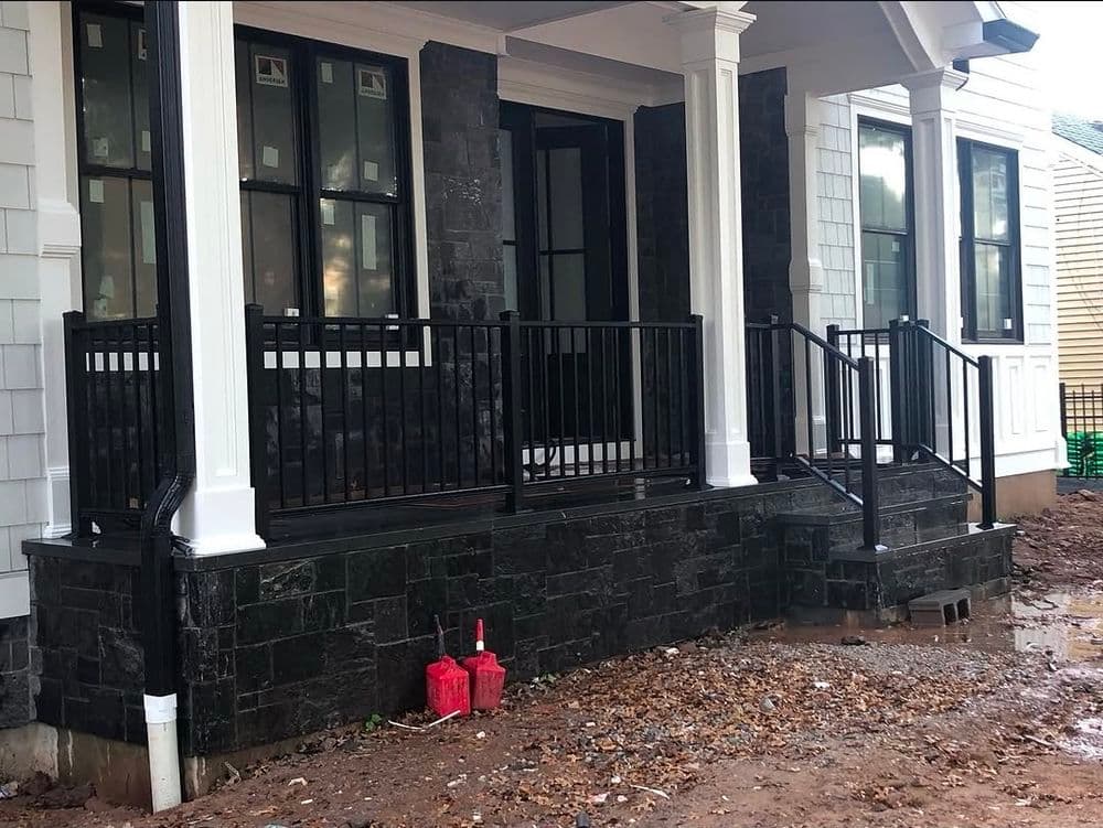 Newly built front porch with black stone, white columns, and black railing. Construction site.