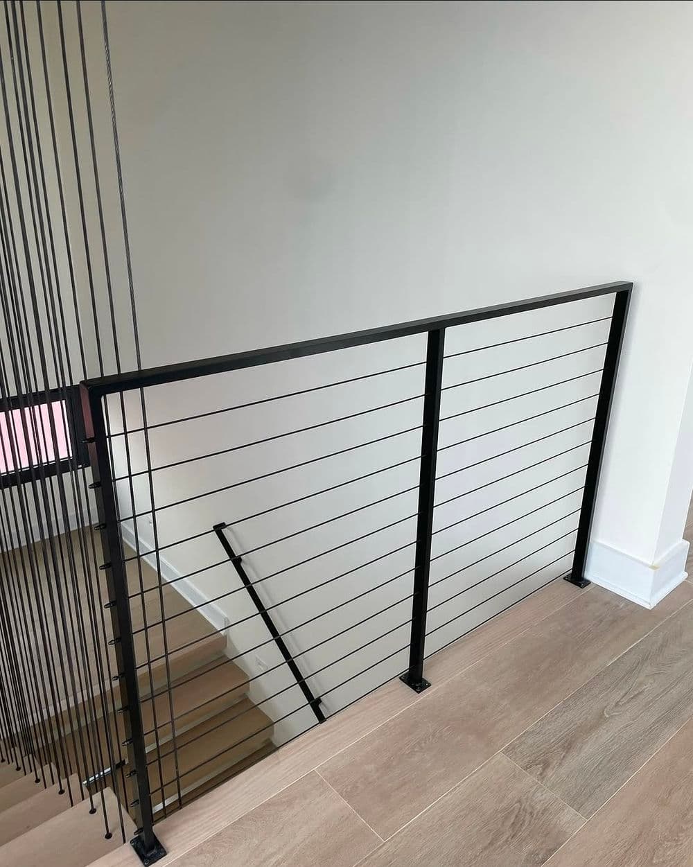 Modern stair railing with sleek black metal and wire design, overlooking wooden stairs.