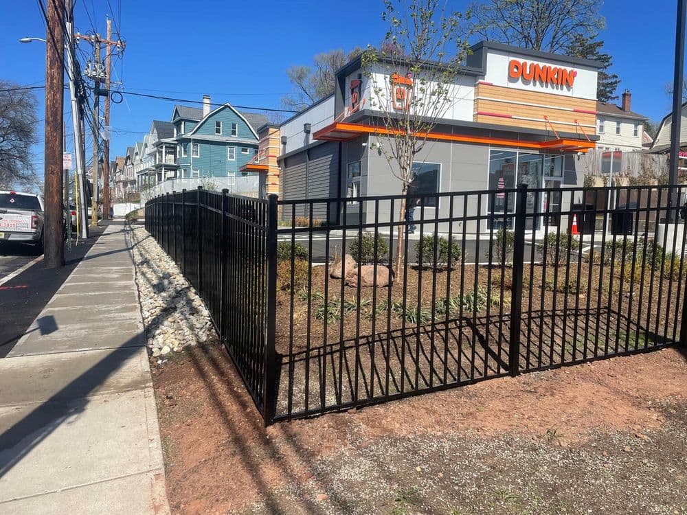 Dunkin' store exterior with black fence and nearby sidewalk on a sunny day.
