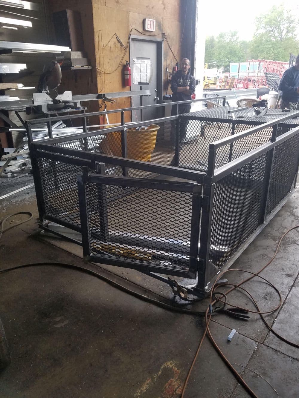 Welded metal cage structure with mesh panels in a workshop setting.