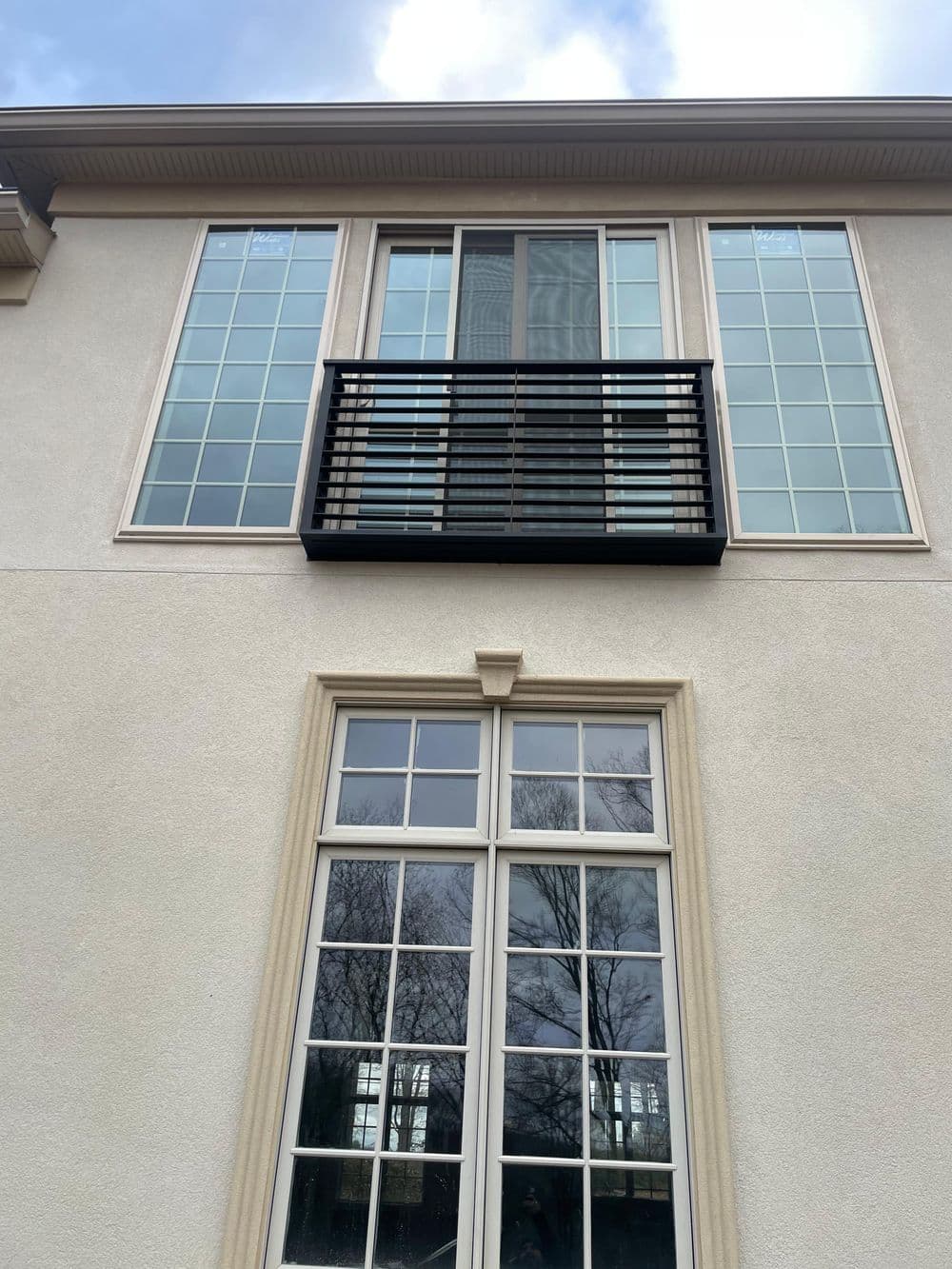 Modern home exterior featuring large windows and a balcony with black railings.