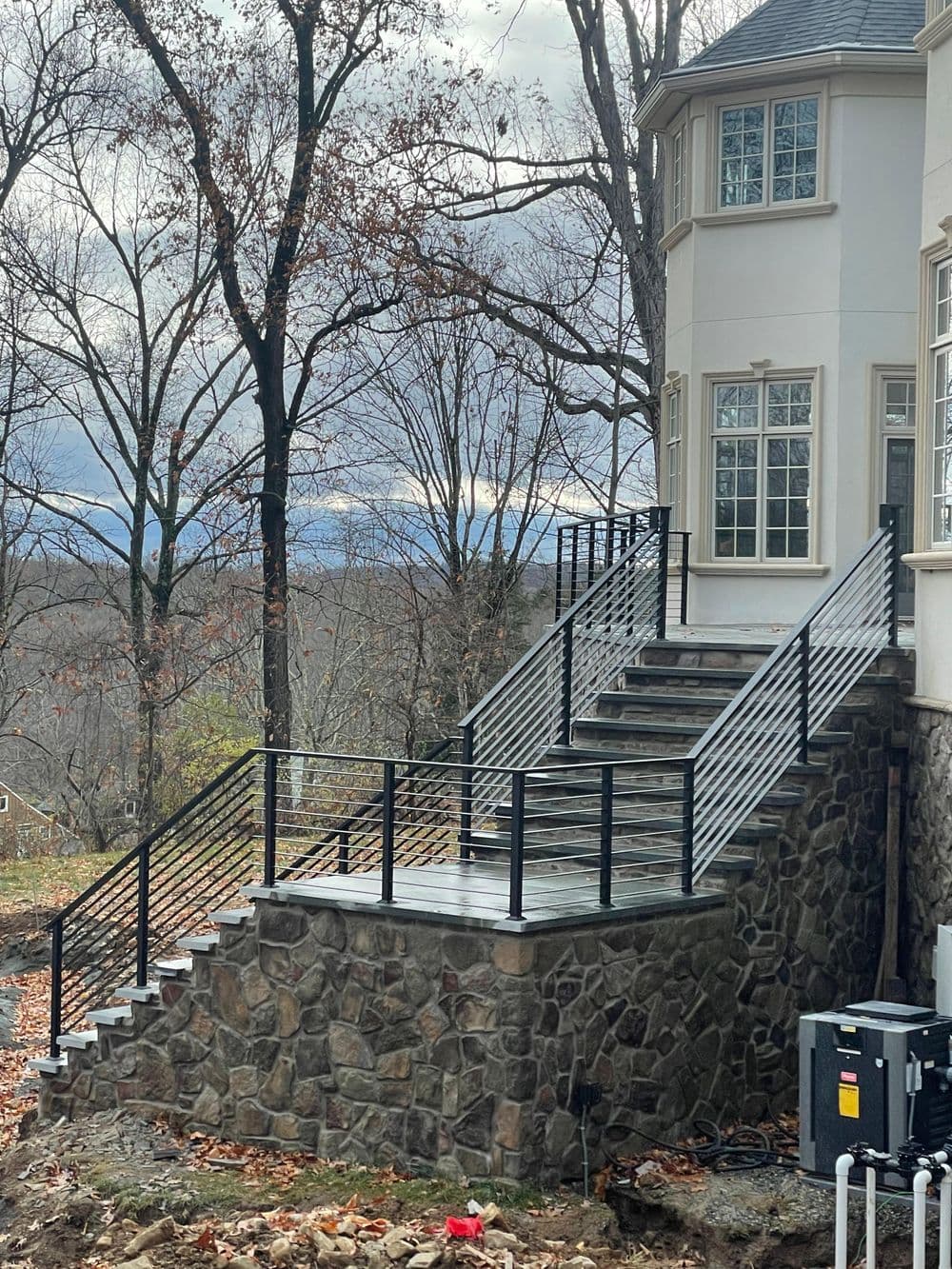 Modern stone staircase with black railings leading to a contemporary home amidst trees.