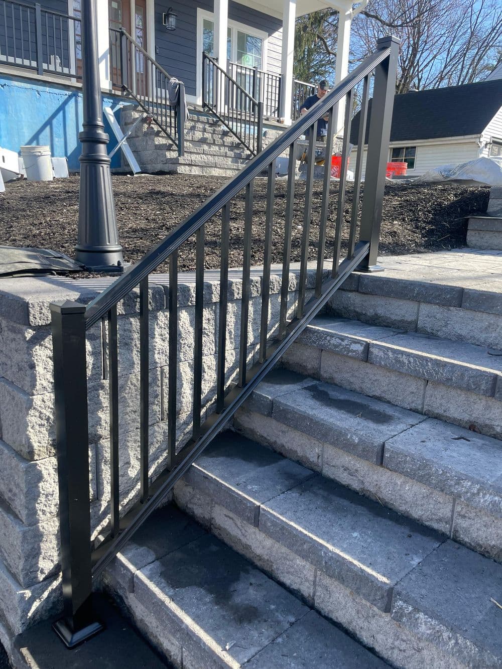 Metal railing installed on stone staircase with modern residential backdrop.