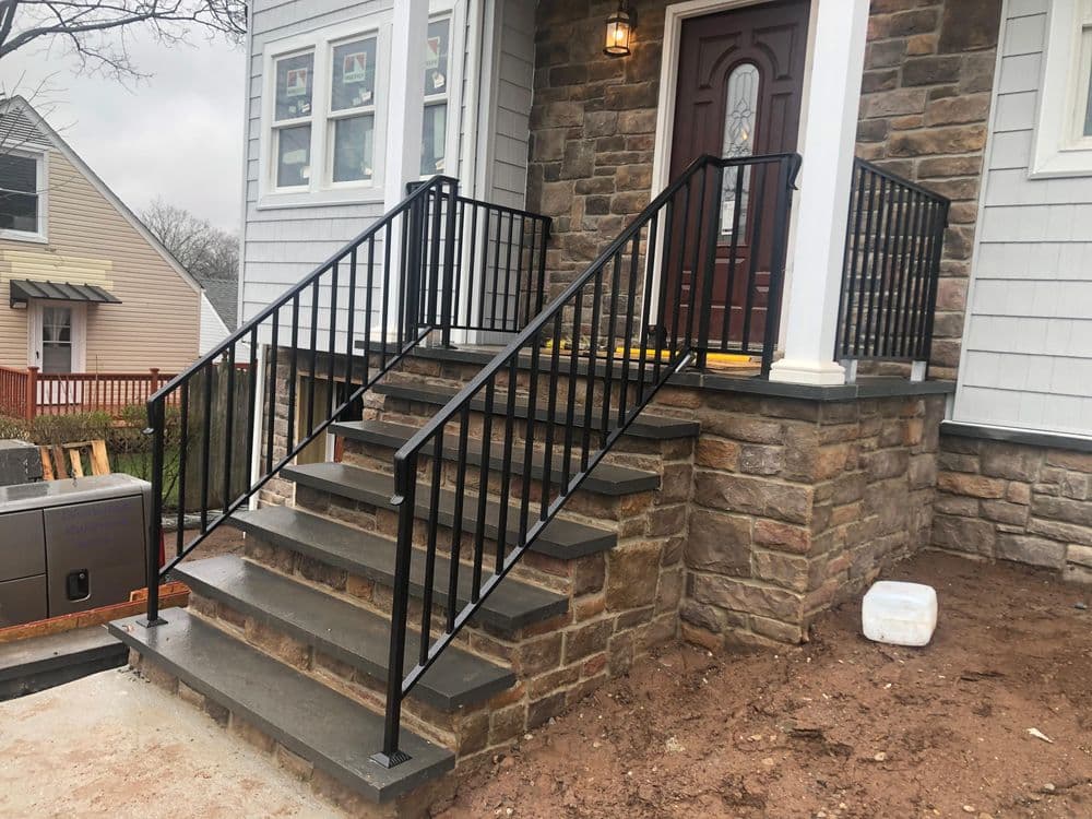 Newly constructed stone steps with black metal railings at a residential entrance.
