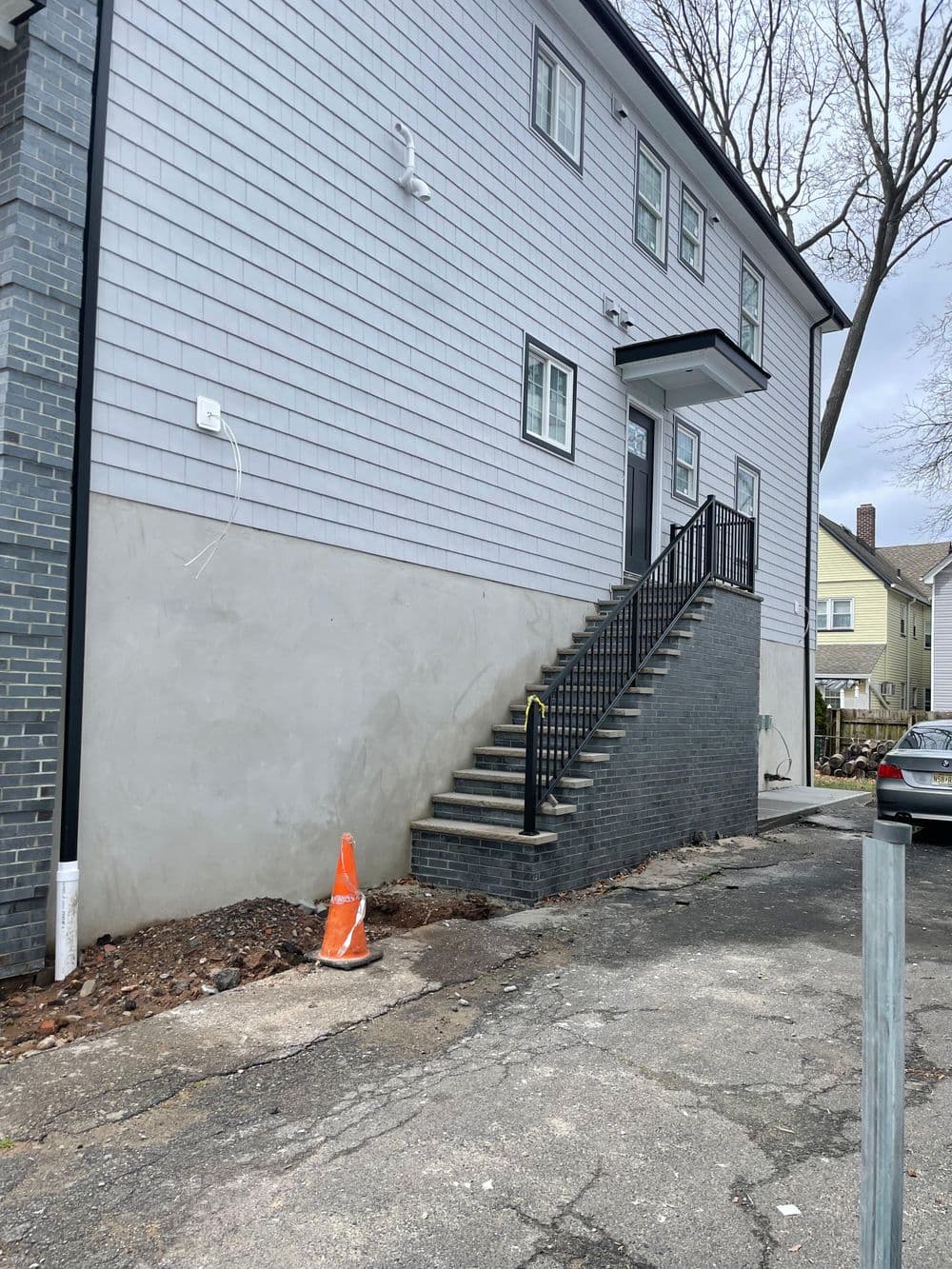 Staircase leading to a gray house with brick and siding, featuring a traffic cone beside it.