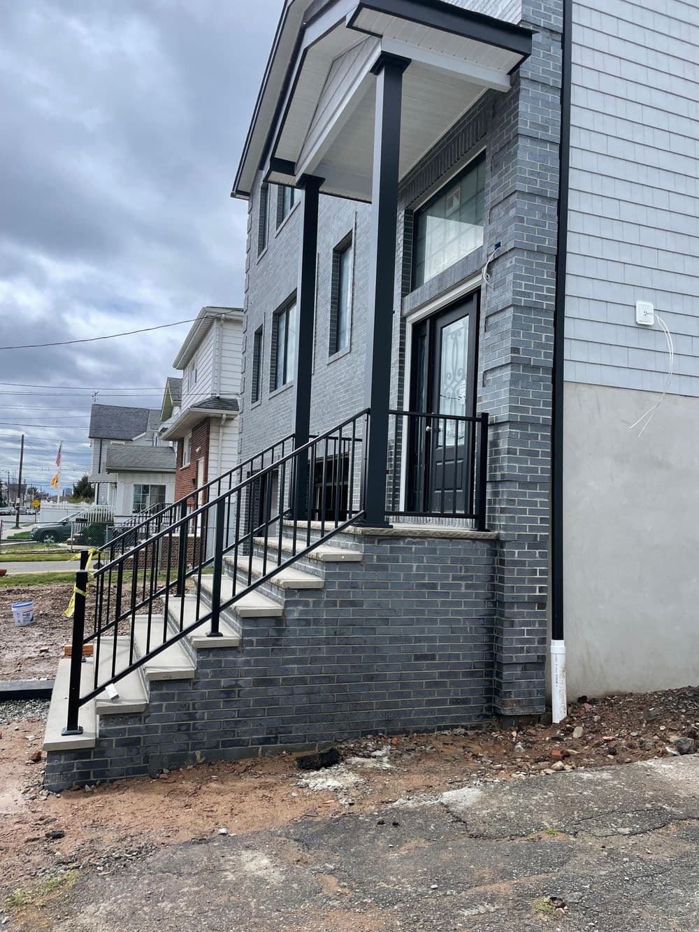 Newly built two-story gray brick home with black railings and concrete steps.
