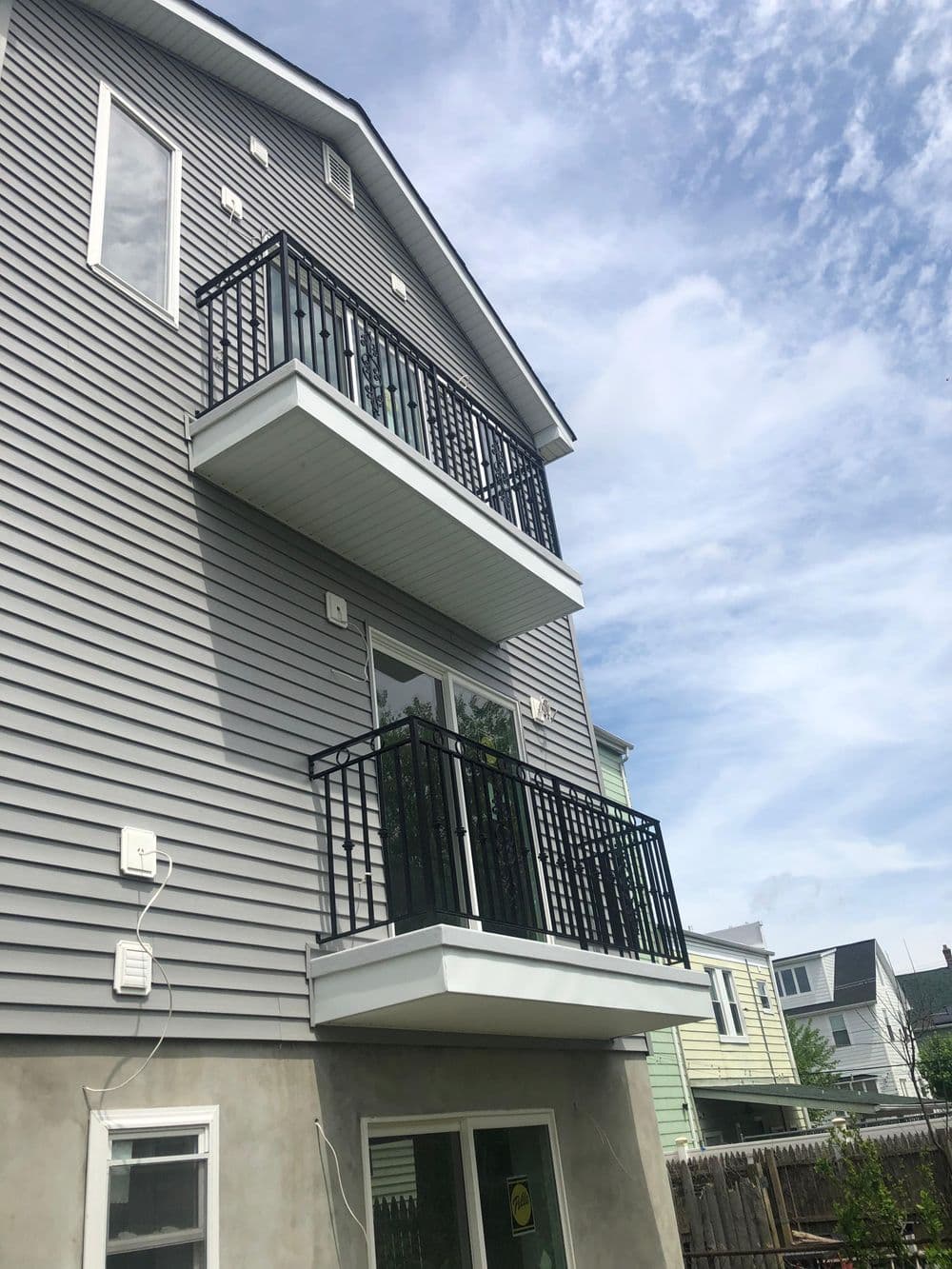 Modern multi-family house with two balconies, gray siding, and clear sky. Perfect for urban living.