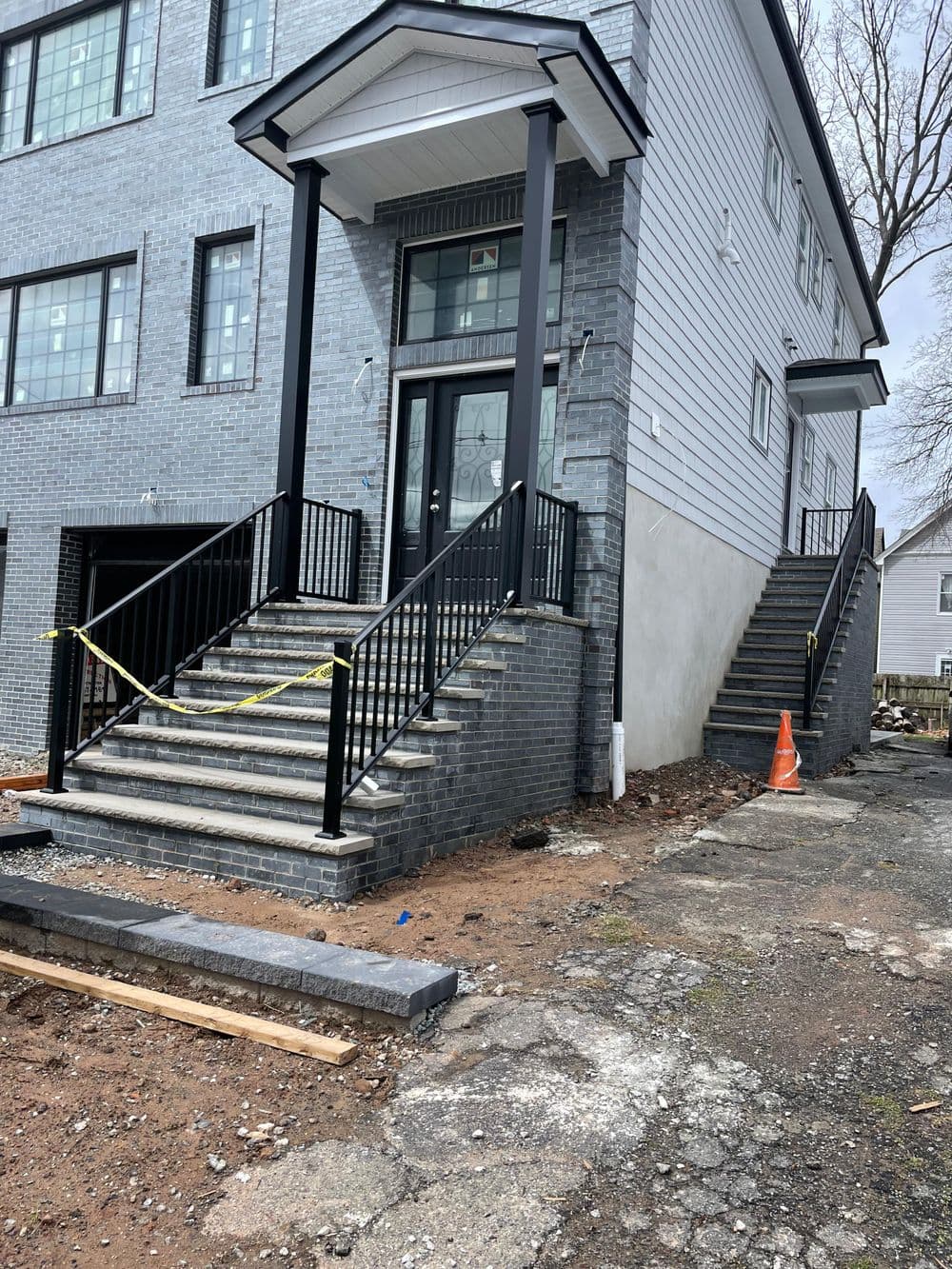 Two sets of stairs leading to a modern gray brick building, under construction with caution tape.