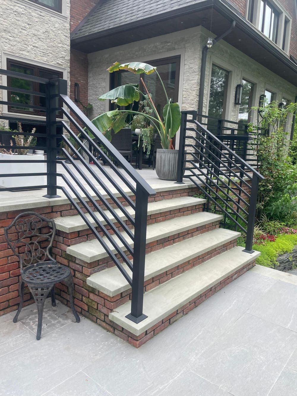 Modern outdoor staircase with black railings and potted plants, surrounded by greenery.