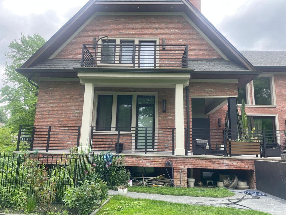 Modern brick house with a covered porch, balcony, and lush garden in front.
