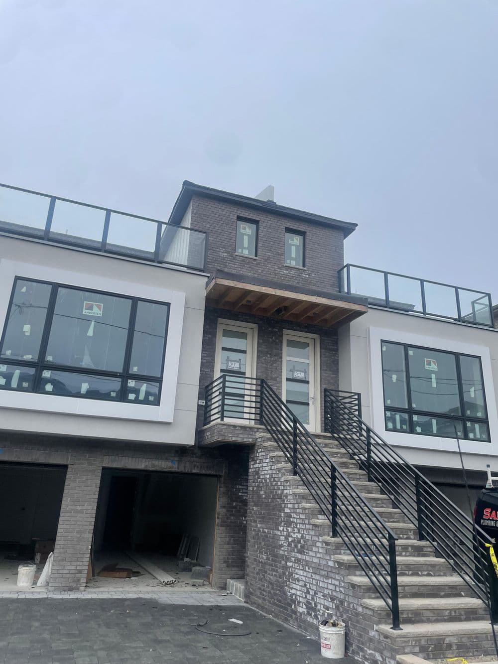 Modern two-story house with large windows, balcony, and stone steps under a cloudy sky.