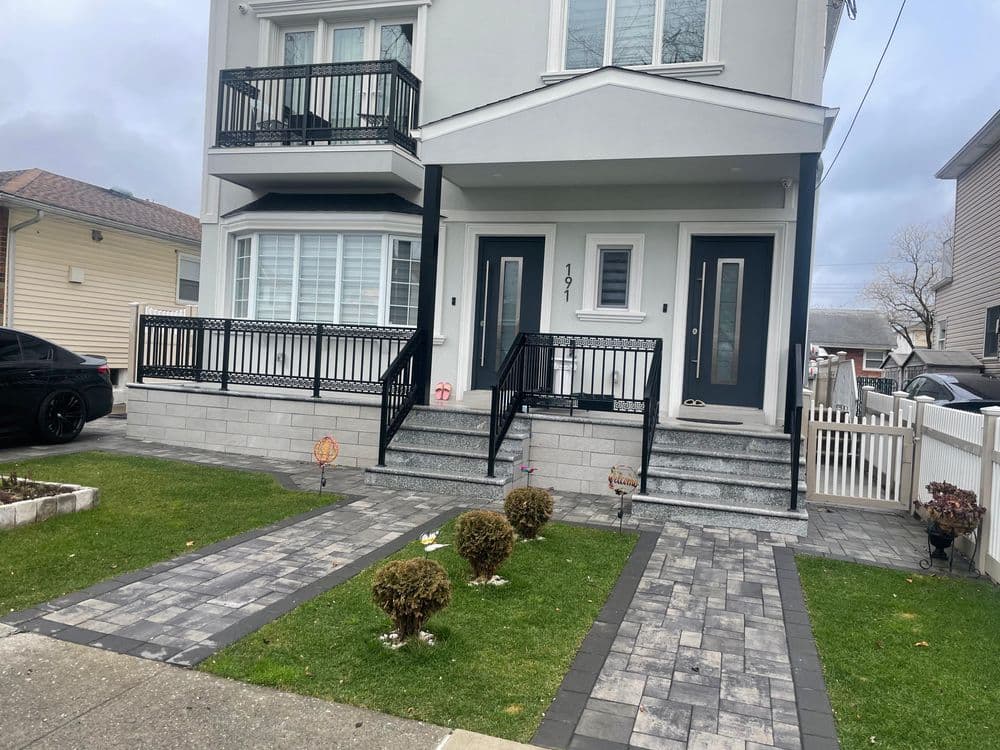 Modern home exterior with landscaped front yard and paving stones, featuring black railings.