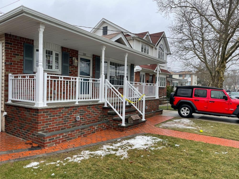 Brick house with a front porch, red Jeep parked out front, and snow on the lawn.