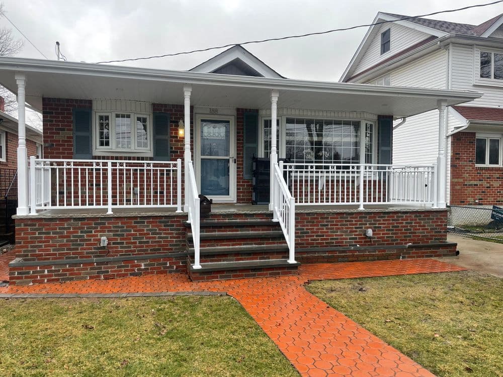 Cozy brick house with a welcoming porch, white railings, and a neatly paved pathway.