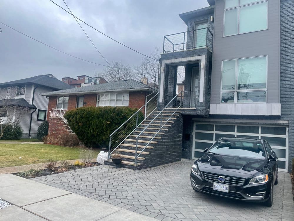 Modern home exterior with stairs, parked black Volvo, and cloudy sky in background.