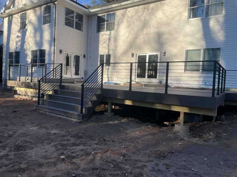 Newly built deck with stairs and railing at a house exterior, featuring modern design elements.