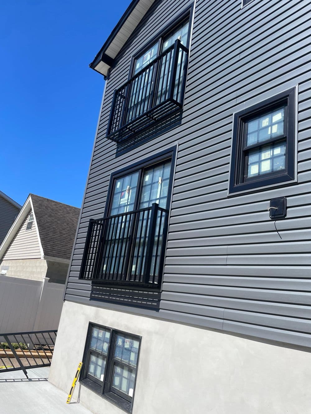 Modern building exterior with black railings, windows, and gray siding under a clear blue sky.