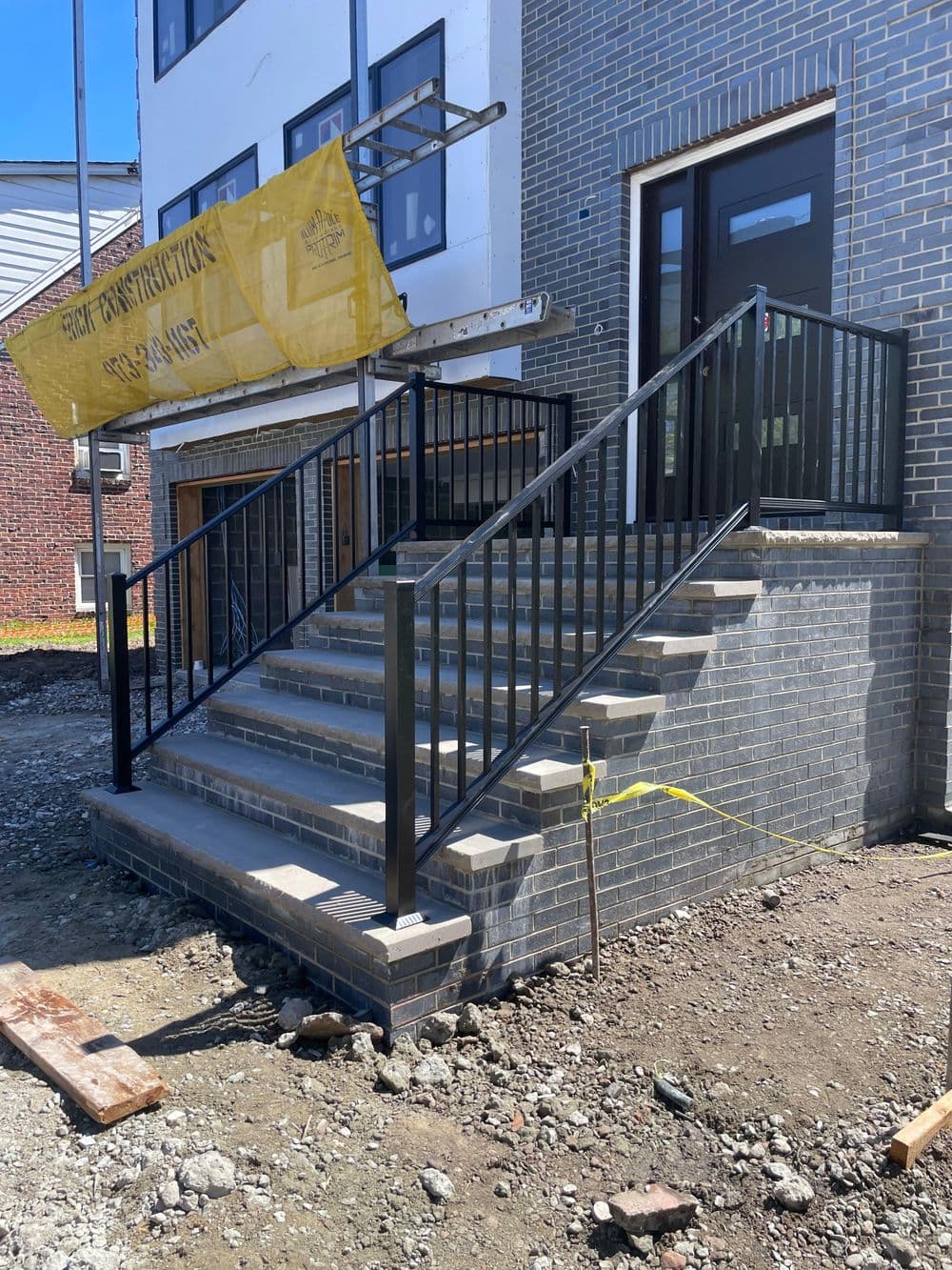 Construction site featuring new brick steps and a black metal railing with safety signage.