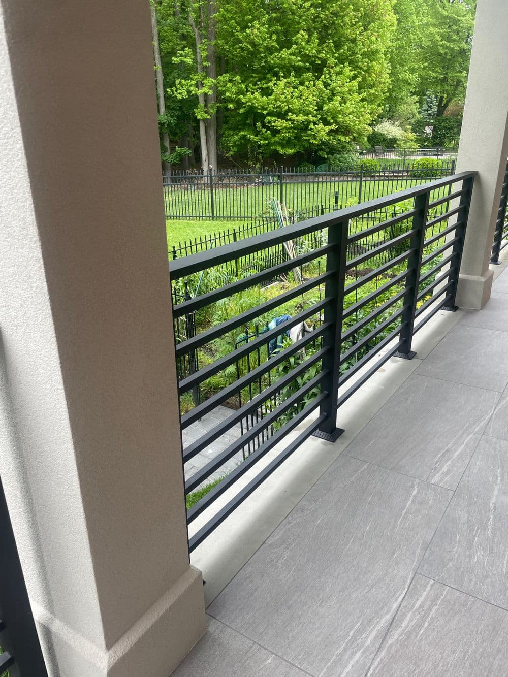 Modern balcony view with black metal railings and lush green landscaping beyond.