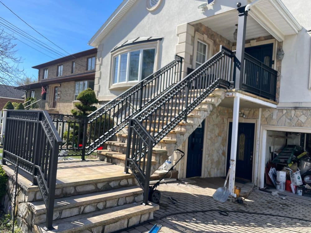 Exterior view of a house with a stone staircase and black metal railings on a sunny day.