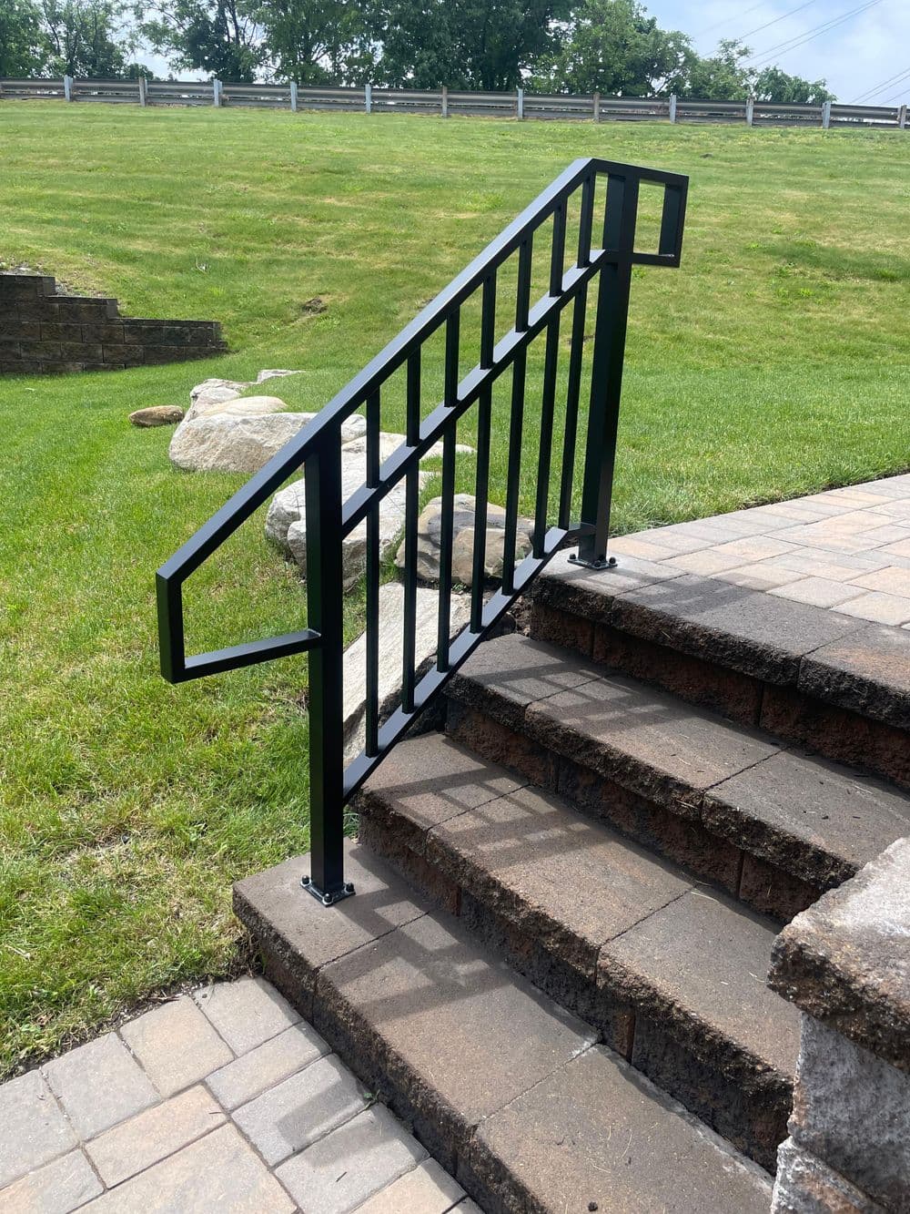 Black metal railing on stone steps in a grassy area, enhancing safety and accessibility.