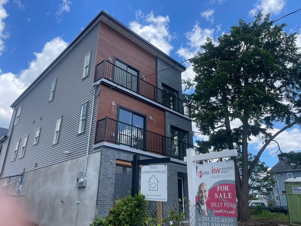 Modern three-story building by Hello Construction, For Sale sign in front, clear blue sky.