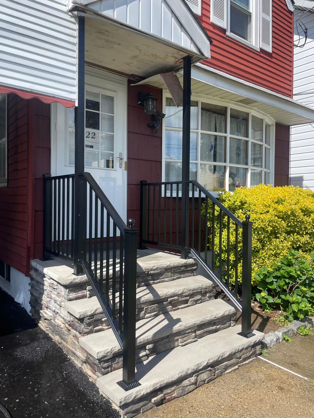 Black metal railings on stone steps lead to a red and white house entrance with a porch.