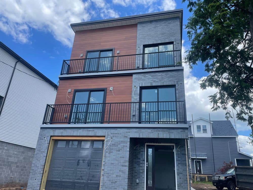 Modern three-story house featuring gray brick and wood paneling, with balconies and a garage.
