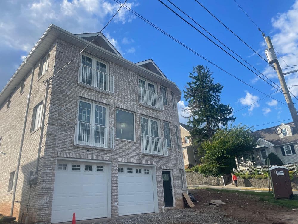 New modern brick house with large windows, garage, and surrounding landscape under a blue sky.