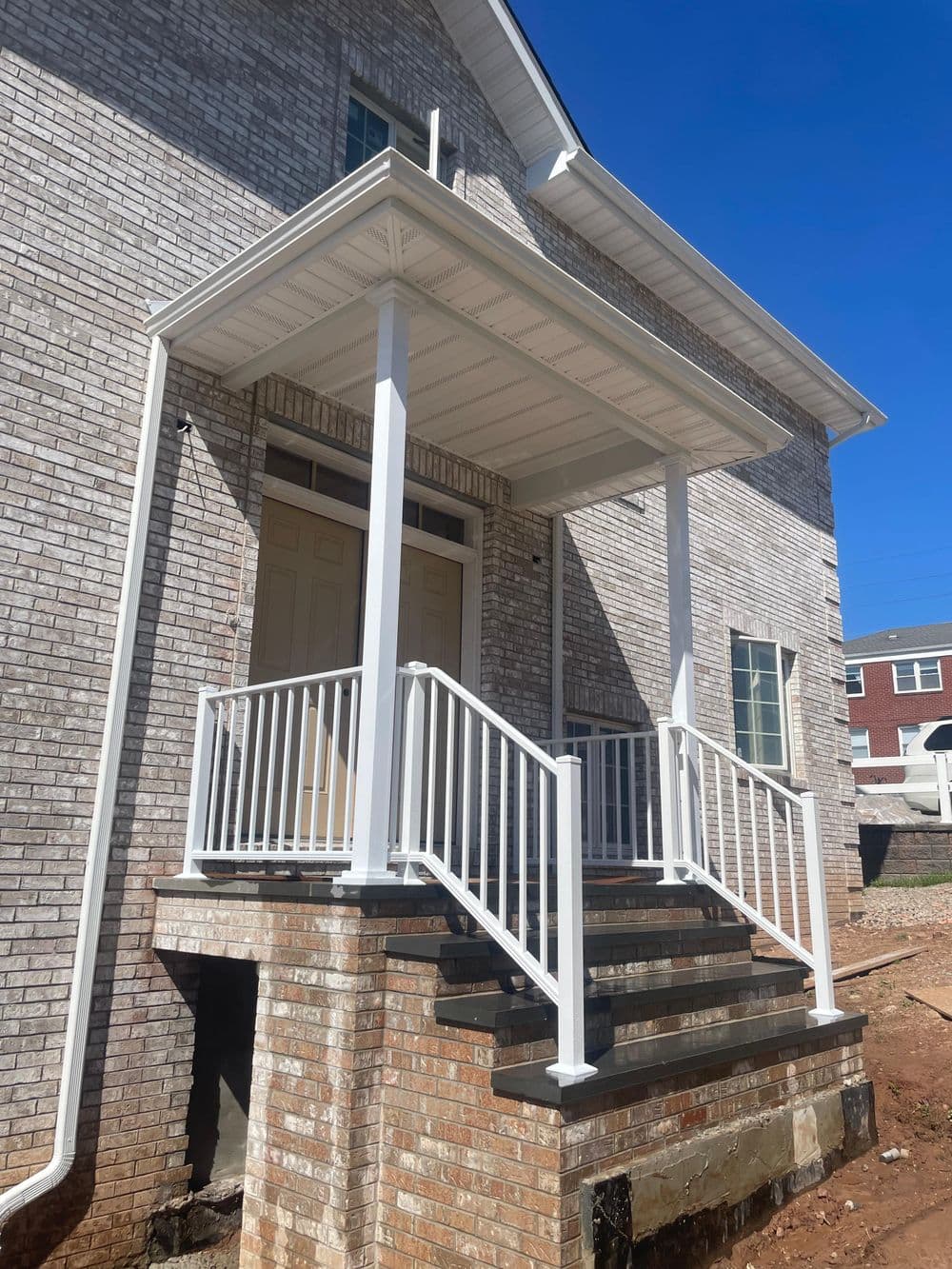 Newly built porch with white railing and steps, brick exterior, clear blue sky background.