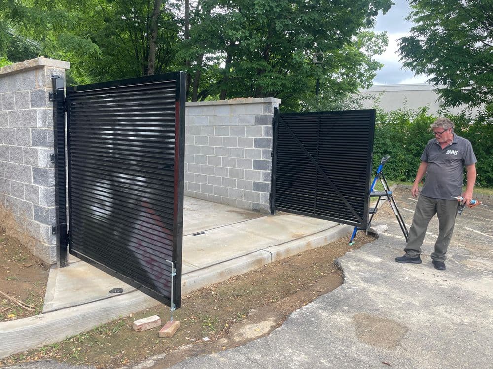 Man inspecting a newly installed black metal gate with a stone wall backdrop.