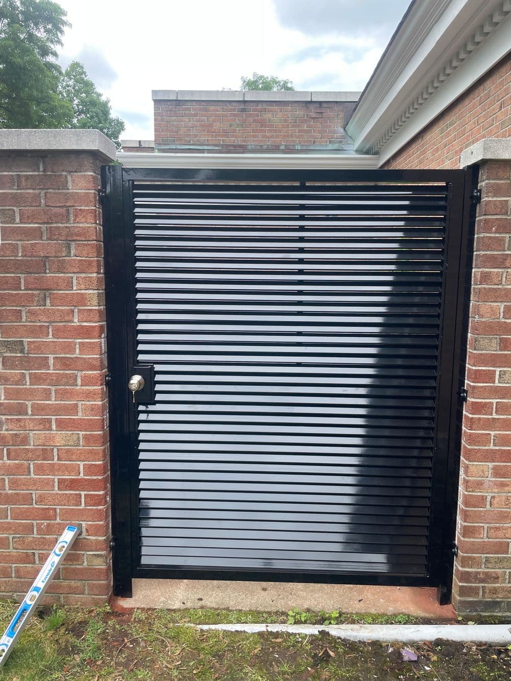 Black horizontal slat gate installed in brick wall, leading to enclosed area.