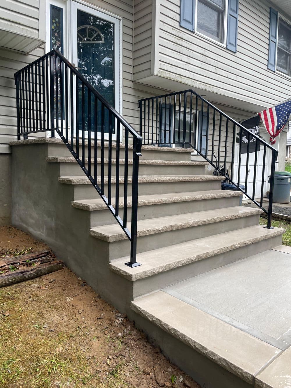 Concrete stairs with black railing and American flag outside a residential home.