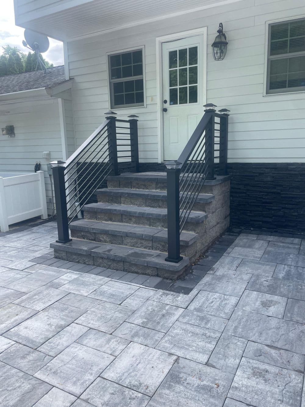 Modern entrance with black railing and stone steps, leading to a white house door.