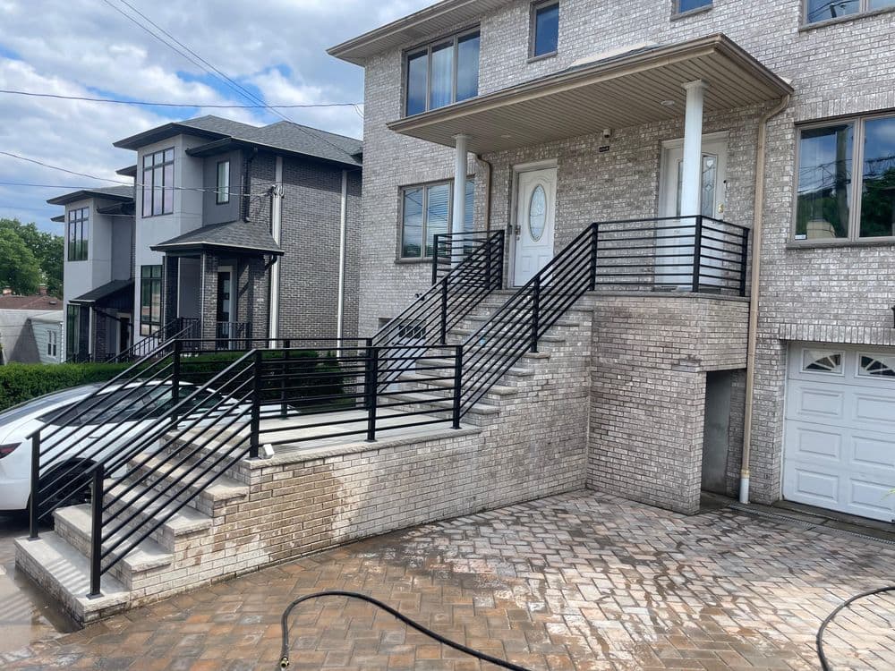 Modern home exterior with stone stairs, black railings, and landscaped entrance.