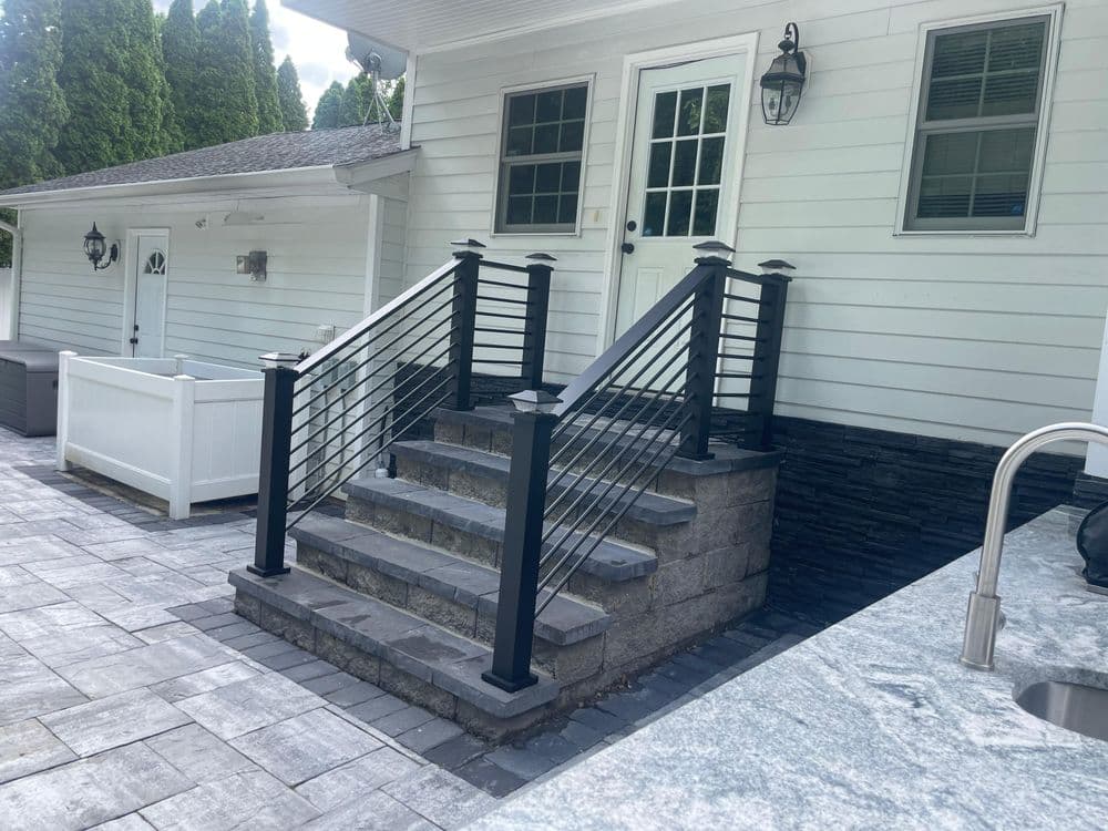 Modern outdoor staircase with black railings, stone steps, and a white house in the background.