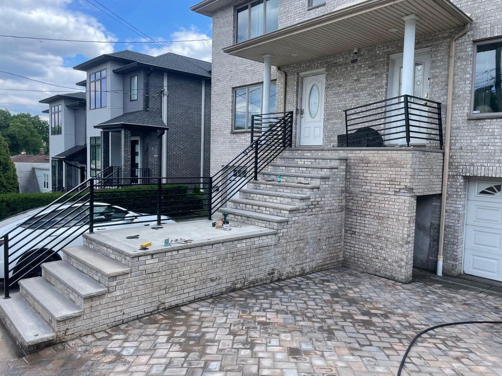 Modern brick home exterior with stairs and railing, featuring a paved driveway.