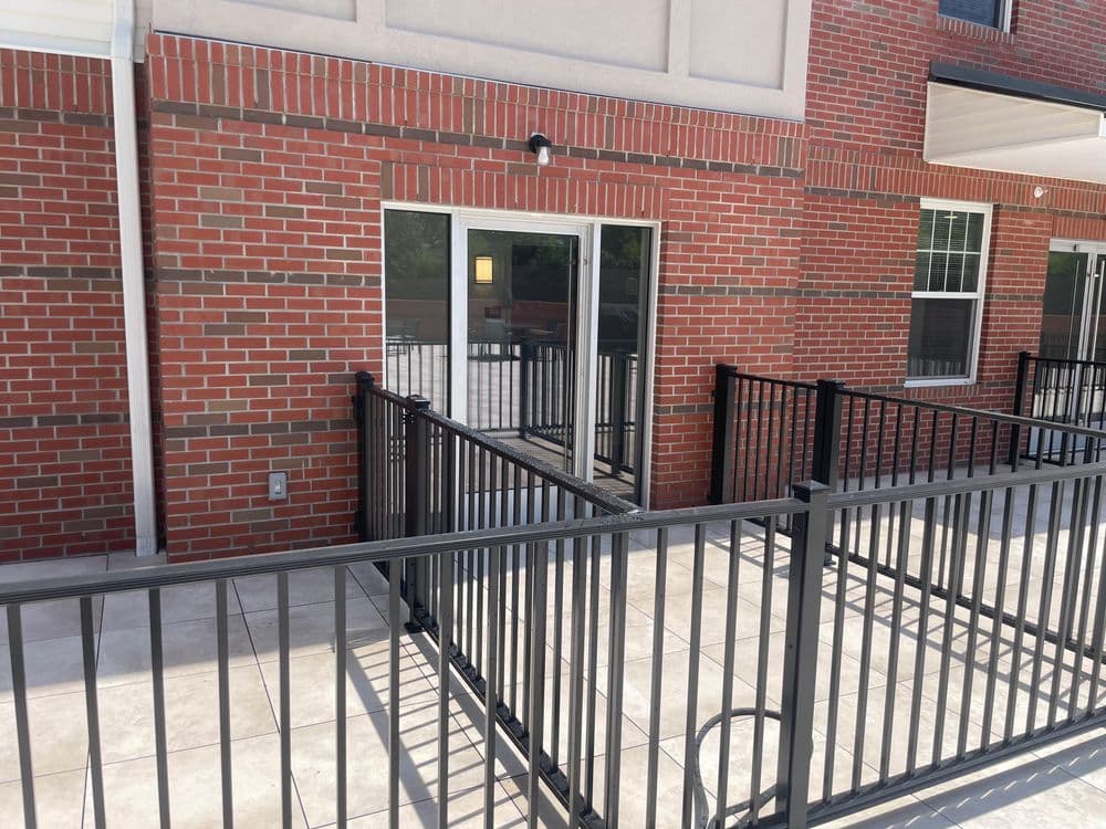 Modern brick building with a patio and black railings, featuring sliding glass doors.