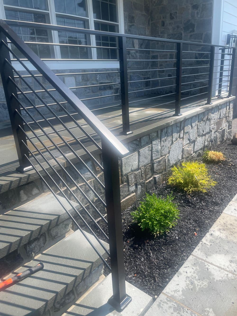 Modern metal railing on stone steps with greenery and a stone facade, adding curb appeal.