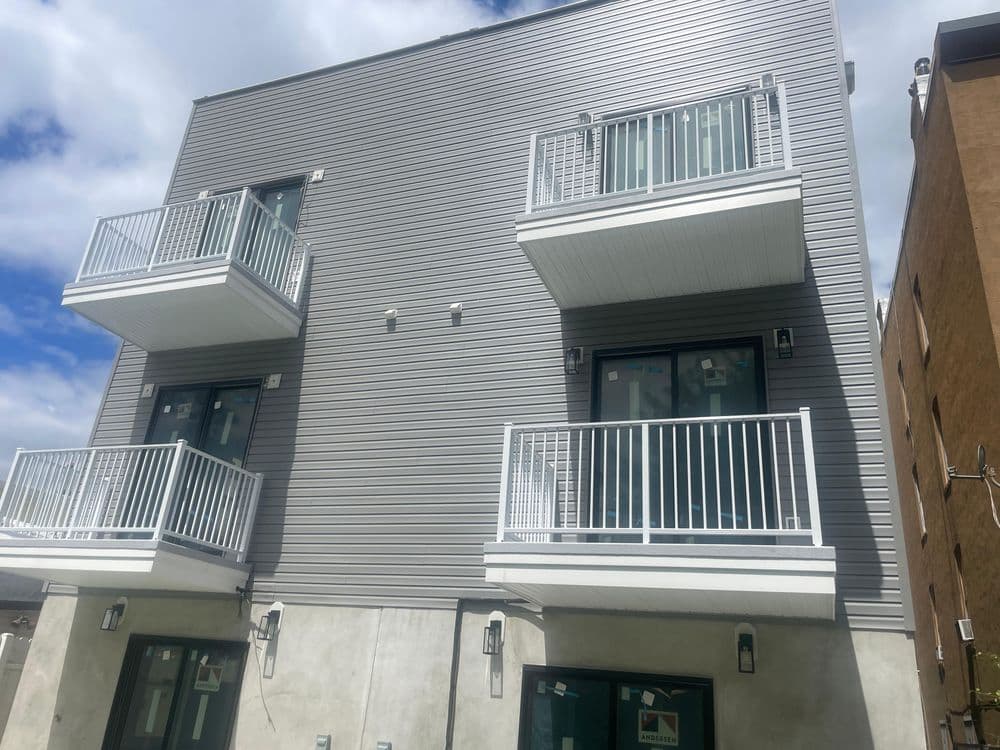 Modern apartment building with balconies and large windows under a cloudy sky.