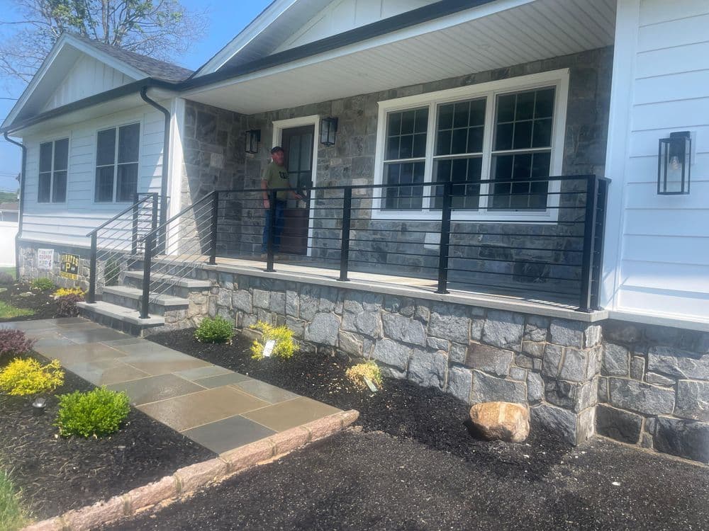Modern home with stone facade, black railing porch, and landscaped entryway.