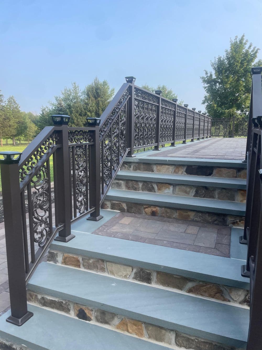 Elegant outdoor staircase with decorative metal railing and stone steps, surrounded by greenery.
