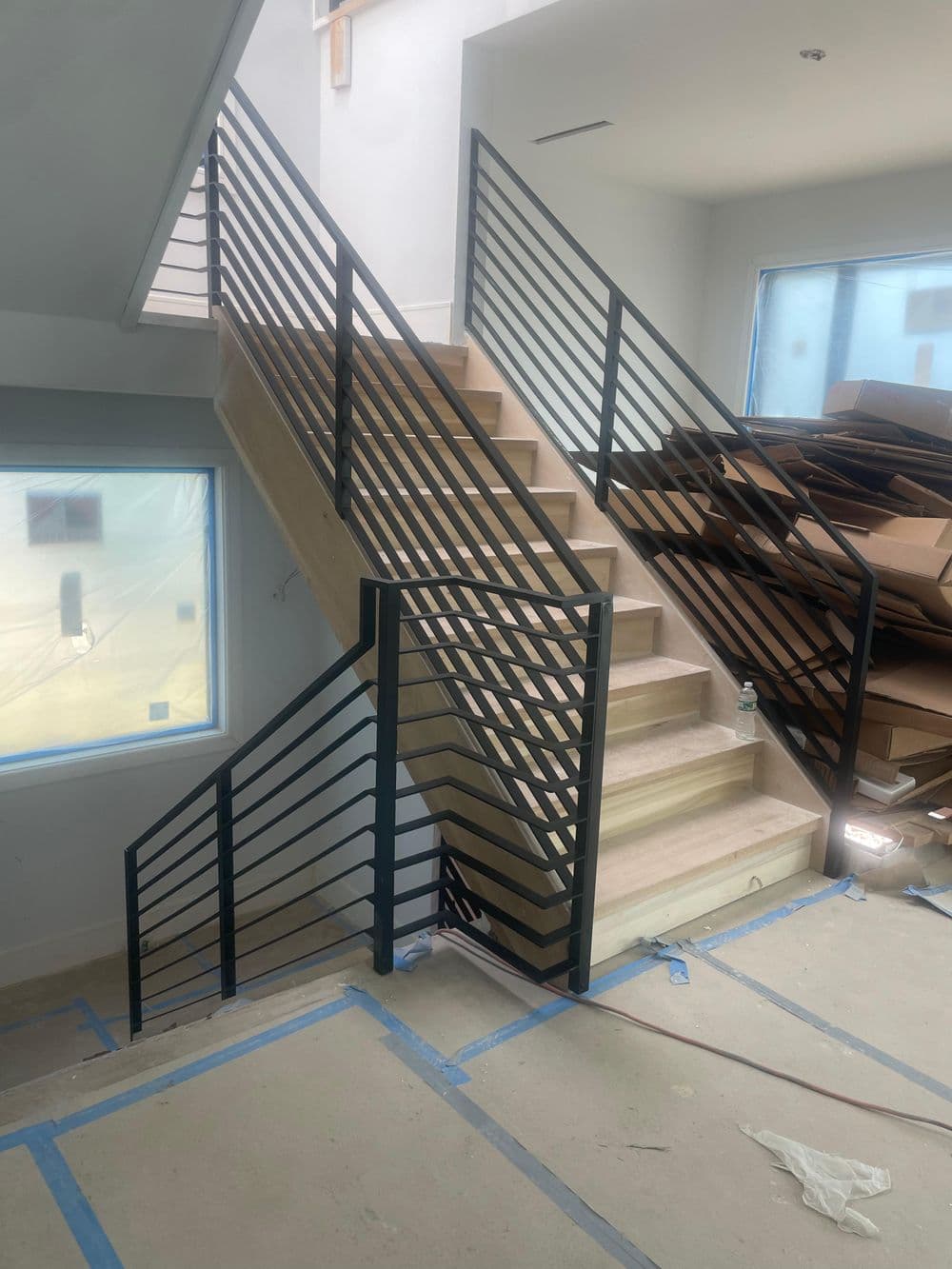 Modern wooden staircase with black metal railing in a partially finished interior space.