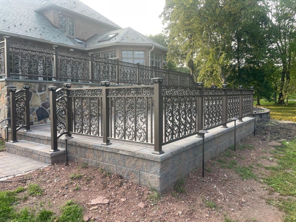 Elegant metal railings surround a stone terrace of a large, upscale house in a scenic setting.