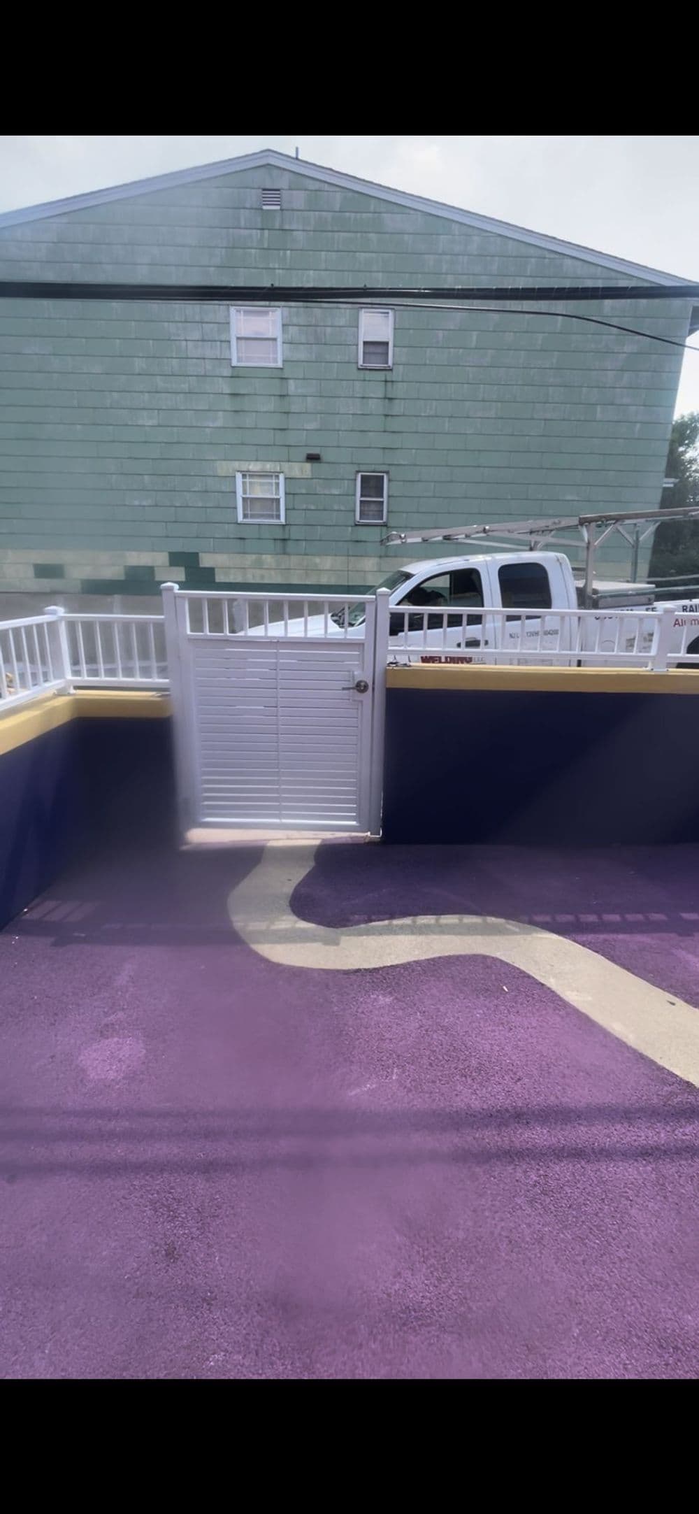 Vibrant purple outdoor area with a white gate and green building in the background.