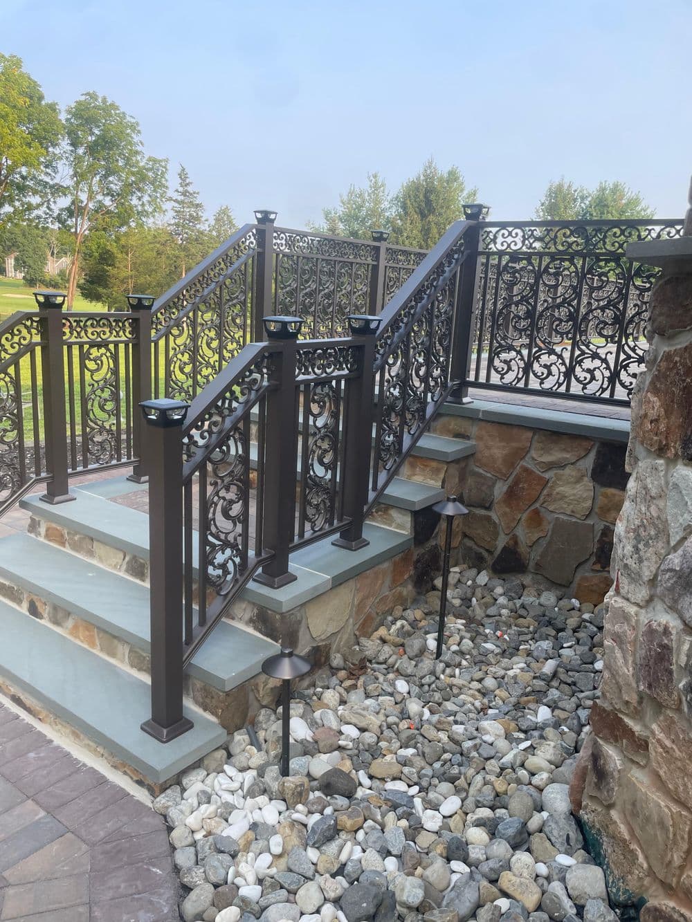Elegant outdoor staircase with decorative metal railing and stone accents in a serene landscape.
