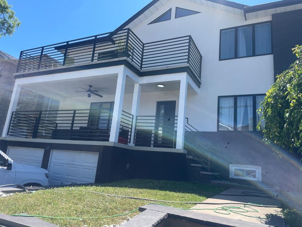 Modern two-story house with a balcony, garage, and landscaped front yard under clear blue sky.