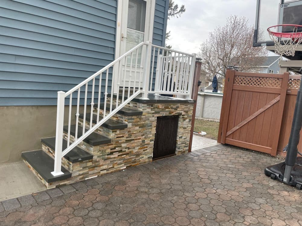 White railing staircase with stone wall leading to a house, basketball hoop in background.