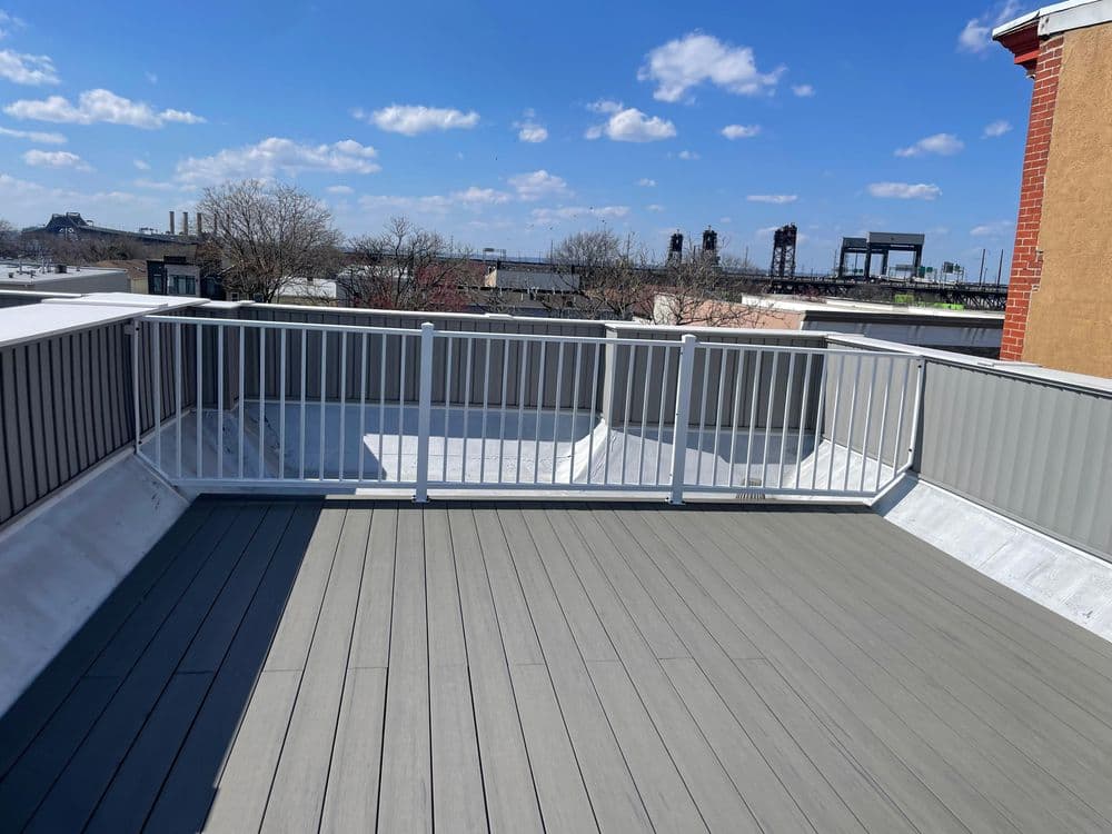 Modern rooftop deck with gray composite flooring and metal railing under a clear blue sky.