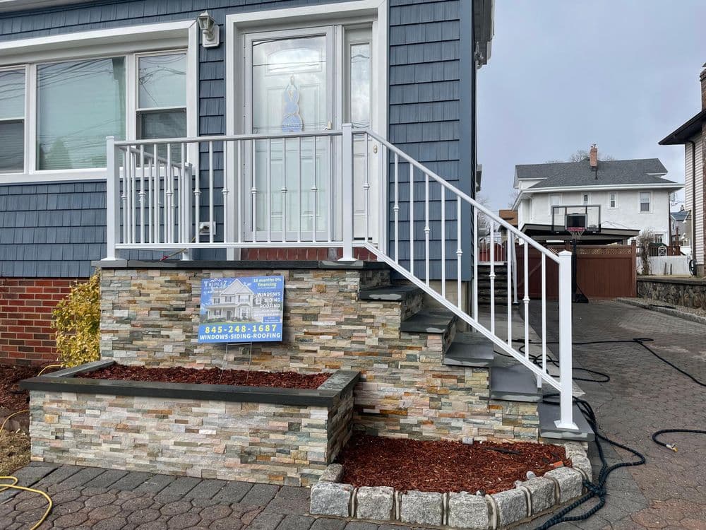 Exterior view of a home featuring a blue facade, stone steps, and white railing.
